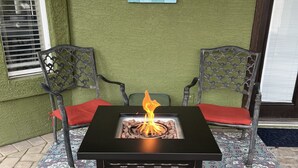 Eine Terrasse mit einem schwarzen Tisch und Stühlen, einer Feuerstelle und einem dekorativen Teppich.