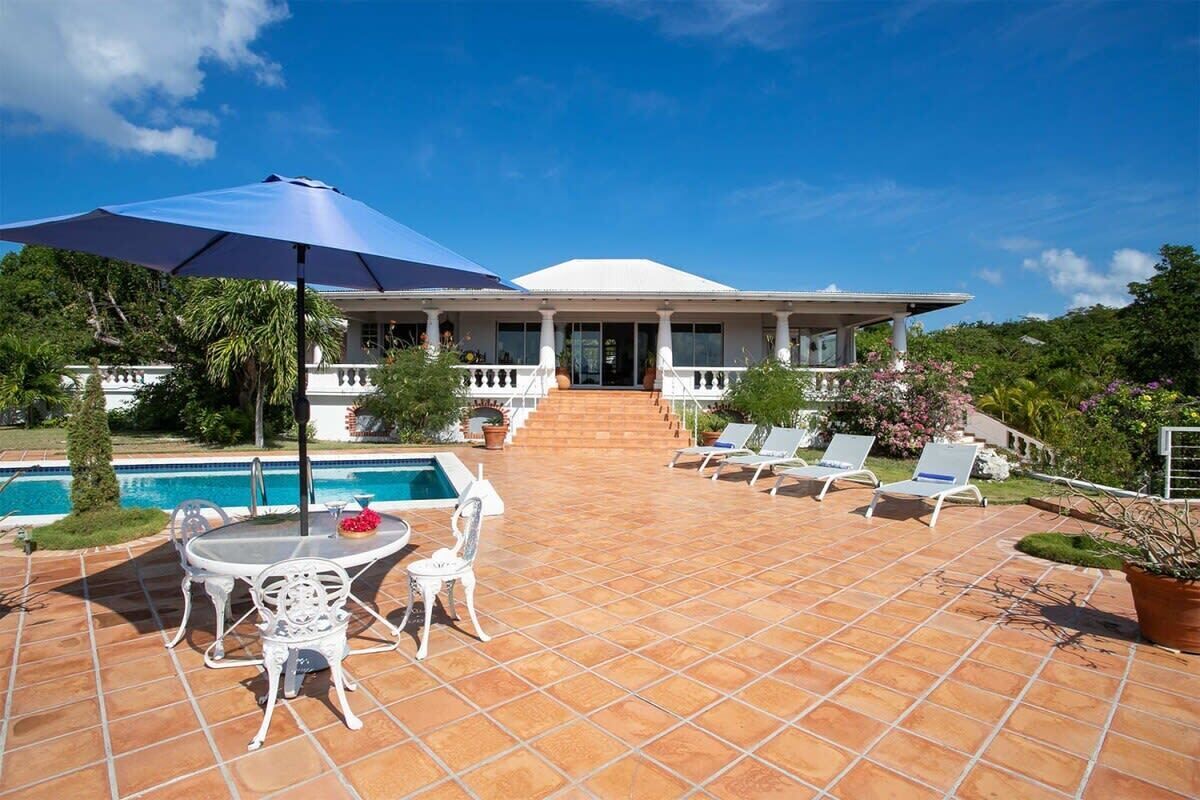 A pool area with a covered seating area, a pool, and a building with a covered porch.