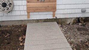 A wooden door with a showerhead, a window with an air conditioning unit, and a small wooden deck.