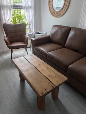 Ett vardagsrum med en brun lädersoffa, ett träbord och en brun läderfåtölj.