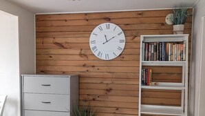 A room with a wooden wall, a white clock, a bookshelf, a cabinet, and a hanging light fixture.