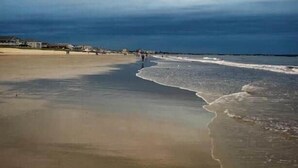 A beach with a wide sandy shore, a calm sea, and a cloudy sky.