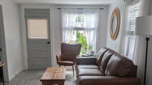 A living room with a brown leather sofa, a wooden coffee table, a wicker ottoman, and a floor lamp.