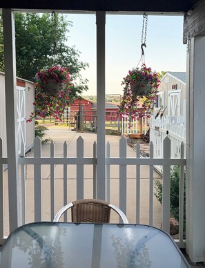 Un espace extérieur abrité, avec une table et des chaises, une clôture blanche en bois et des jardinières suspendues.