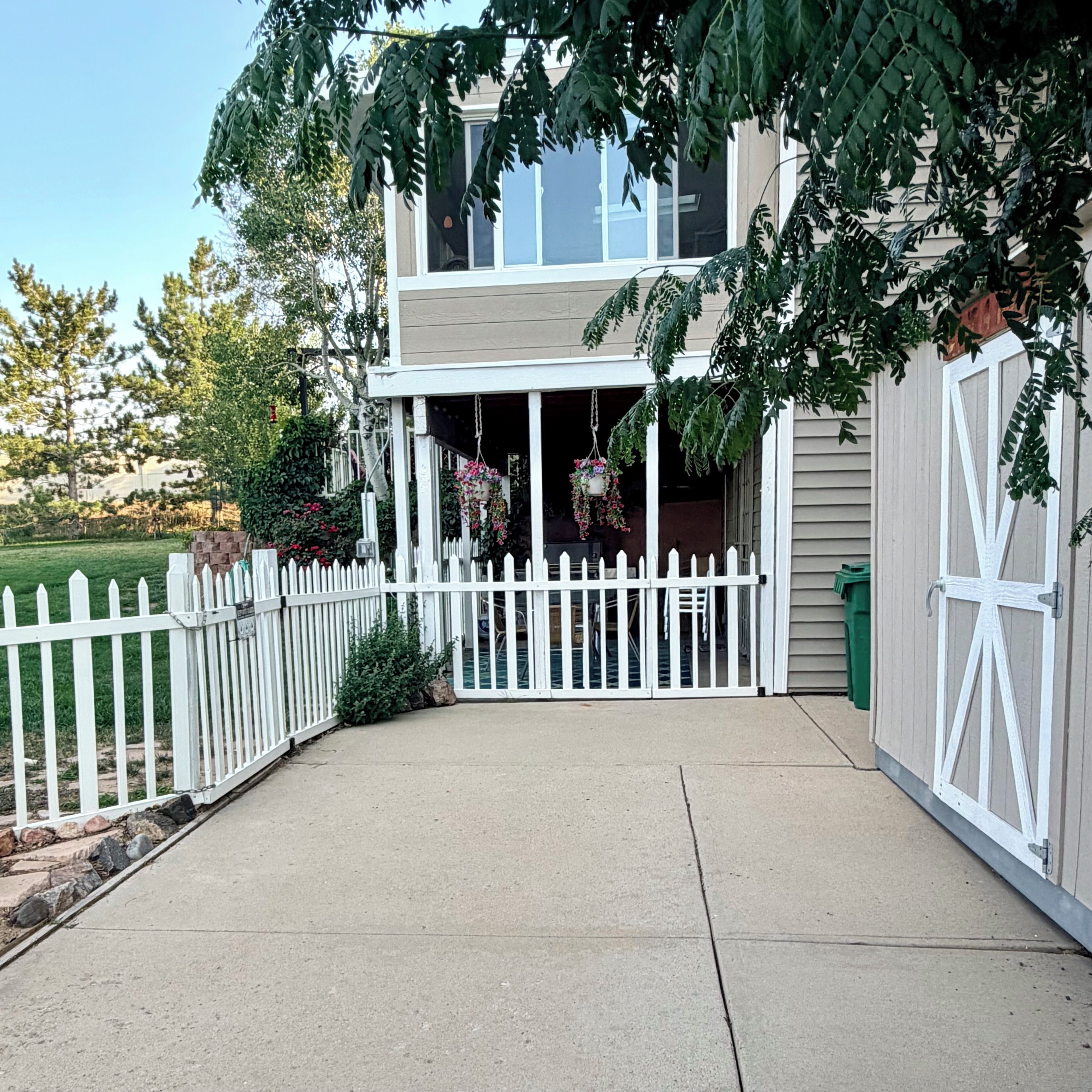A two-story house with a white picket fence, a covered porch, and hanging flower baskets.