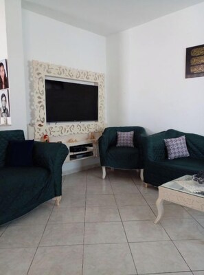 A living room with two green sofas, a flat-screen TV, and a decorative wall piece. - Maison Pieds Dans L'eau à Kelibia (Nabeul)