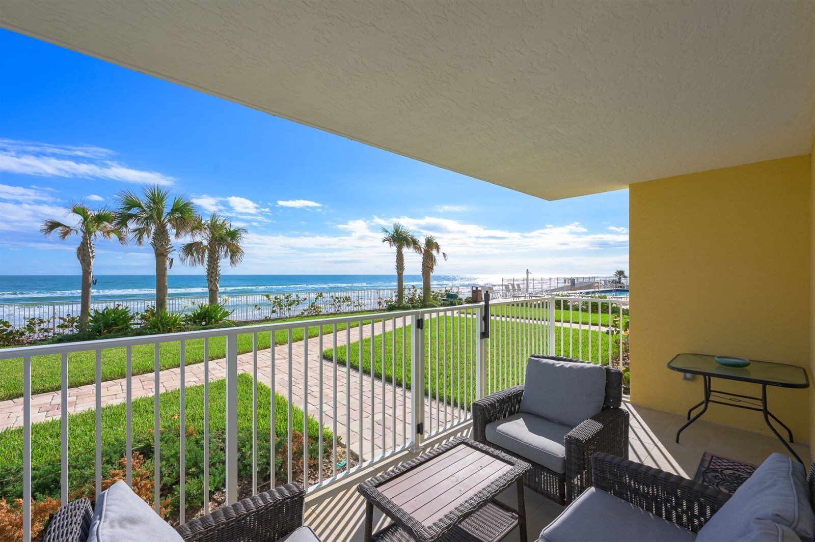 Un balcone con mobili in vimini, vista sulla spiaggia e cielo sereno.