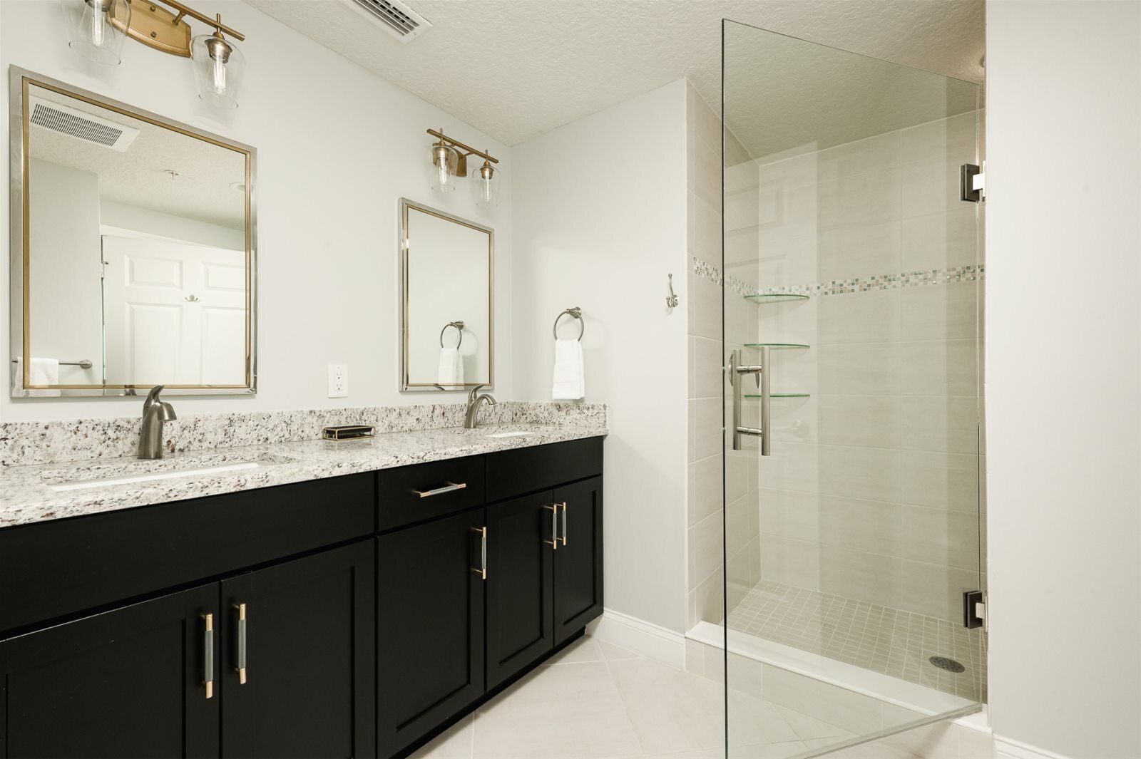 A modern bathroom with a glass-enclosed shower, a double vanity with black cabinets, and two wall-mounted mirrors with light fixtures.