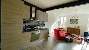 Una cocina moderna con armarios de madera y salpicadero negro, un sofá rojo y un comedor con mesa y sillas de madera.