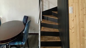 Un interior moderno con una escalera de madera, una zona de comedor con una mesa redonda y sillas azules, y una pared blanca.