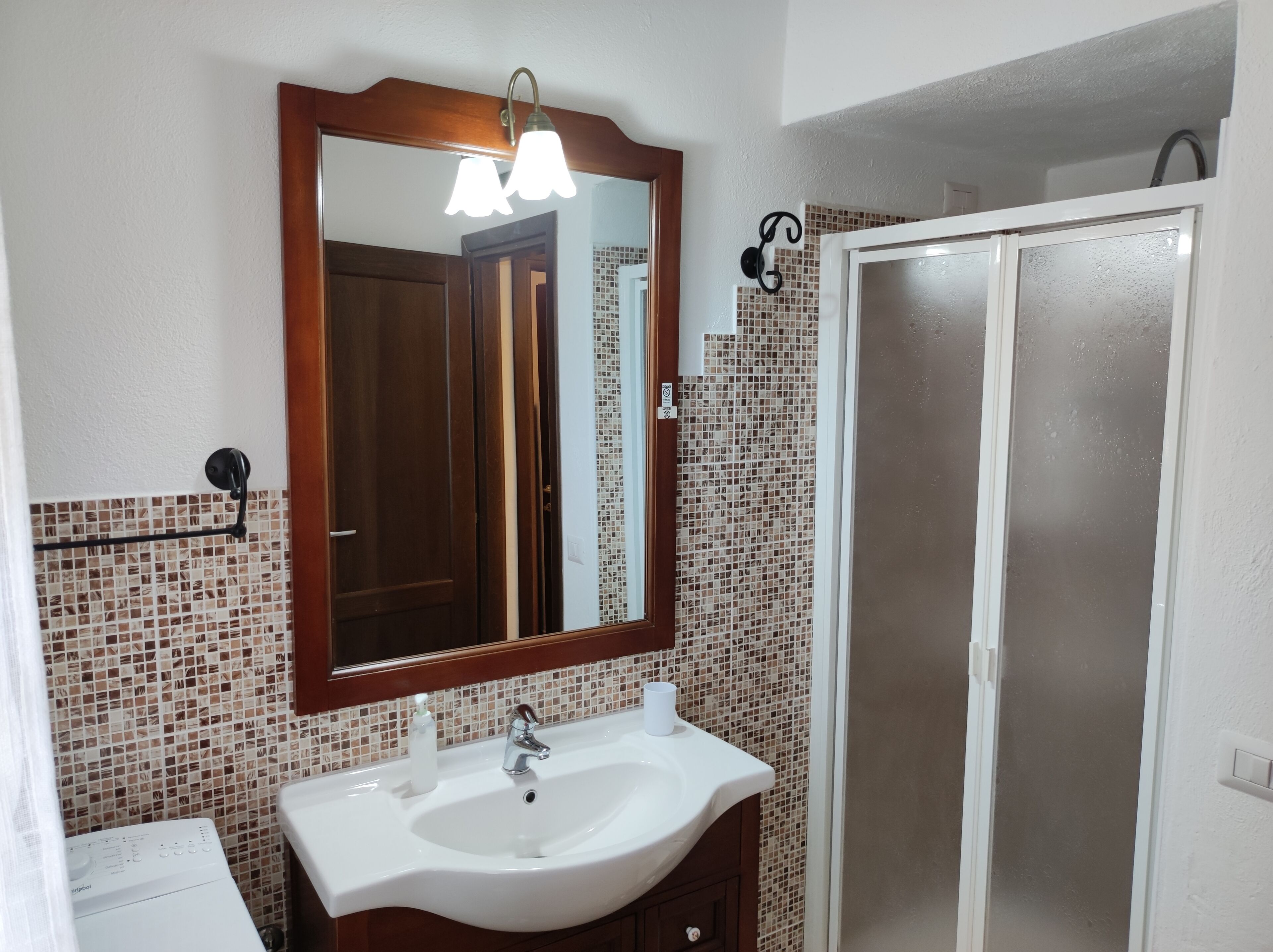 A bathroom with a white sink, a mirror with a wooden frame, a shower with frosted glass doors, and mosaic tile walls.