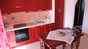Une cuisine avec des meubles de couleur rouge, un plan de travail blanc, une cuisinière, un évier et une table à manger avec des chaises.