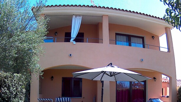 Un bâtiment à deux étages doté d’un patio couvert, de deux chaises longues et d’un grand parasol.
