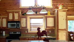 A wooden cabin kitchen with granite countertops, a stainless steel stove, a microwave, and a rooster decoration.