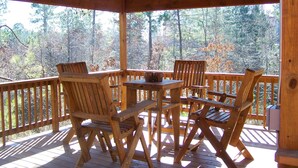 A wooden deck with four chairs and a table, overlooking a forested area.