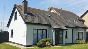Une maison à deux étages, dotée d’un toit en pente, de grandes fenêtres et d’une pelouse bien entretenue.