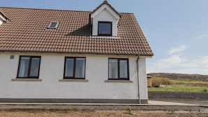 A two-story house with a brown tiled roof, white exterior walls, and three windows. - Woodburn Cottage (Waternish)
