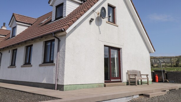 A two-story building with a tiled roof, a large window, and a door. - Woodburn Cottage (Waternish)