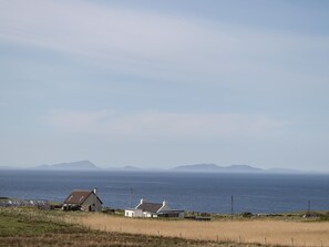 A coastal landscape with houses and a view of the sea and distant mountains. - Woodburn Cottage (Waternish)