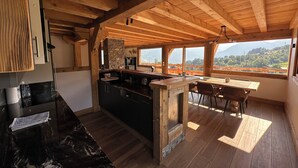 A rustic kitchen with wooden beams, a stone accent wall, and a view of a mountainous landscape. - Chalet Mont Blanc view with outdoor jacuzzi (Combloux)