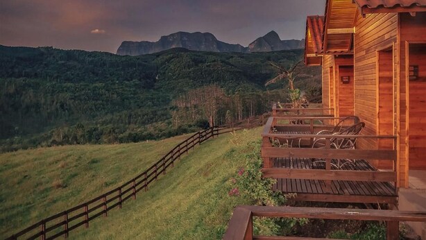 A wooden cabin with a wooden deck and a view of mountains. - Pousada Rio Túnel (Grão Pará)