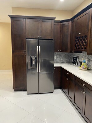 A kitchen with dark wooden cabinets, a stainless steel refrigerator, a tiled backsplash, and a white countertop.