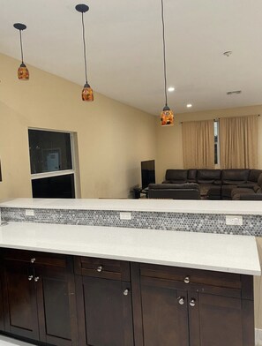 A modern kitchen with a white countertop, dark wooden cabinets, and pendant lighting.