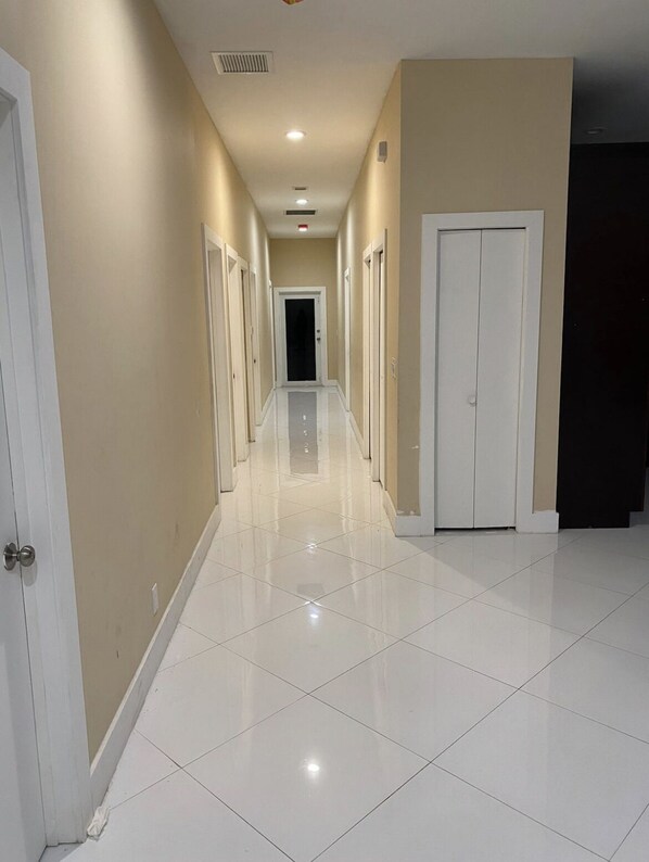 A long, narrow hallway with white tiled floors and beige walls.