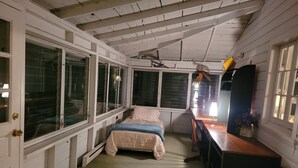 Una habitación pequeña con cama, escritorio y ventanas amplias.