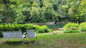 Un conjunto de banco y silla dispuesto en una zona verde con vistas a un río, rodeado de un bosque denso.