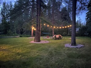 Un espace extérieur verdoyant, avec des arbres, un hamac et des guirlandes lumineuses.