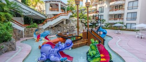 A water park with slides shaped like an elephant and a crocodile, surrounded by a pool and a building with balconies.