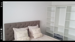 Un dormitorio con cabecera capitonada, cama con ropa de cama estampada y un armario blanco con varios estantes.