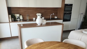 Una cocina moderna con armarios blancos, una isla de madera y una mesa redonda de madera con sillas.