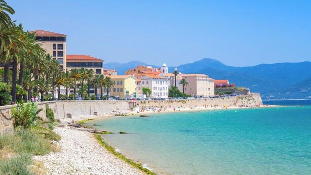 Un pueblo costero con una playa, edificios y montañas al fondo.