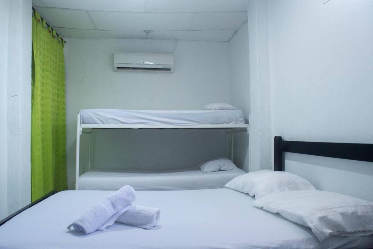 A bunk bed room with a green curtain, white bedding, and an air conditioning unit.