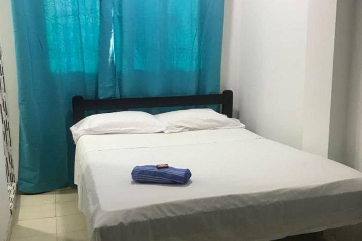 A single bed with a white mattress and pillows, a blue towel, and teal curtains.