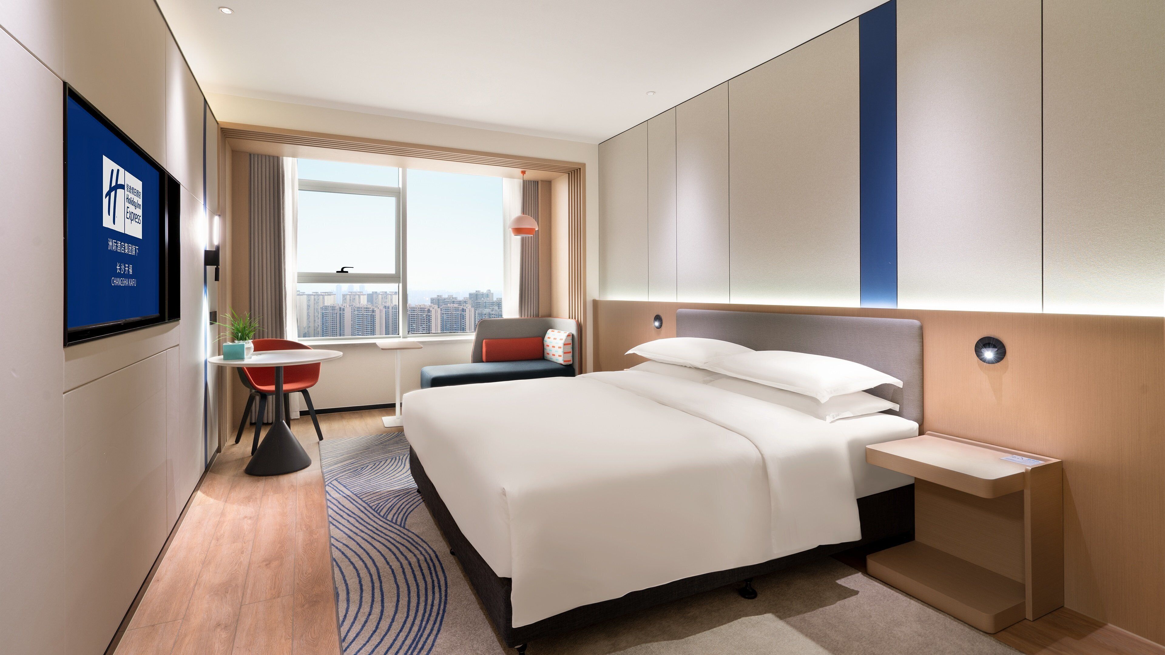 Habitación de hotel con una cama grande, un escritorio, una silla, un televisor y vistas a la ciudad.