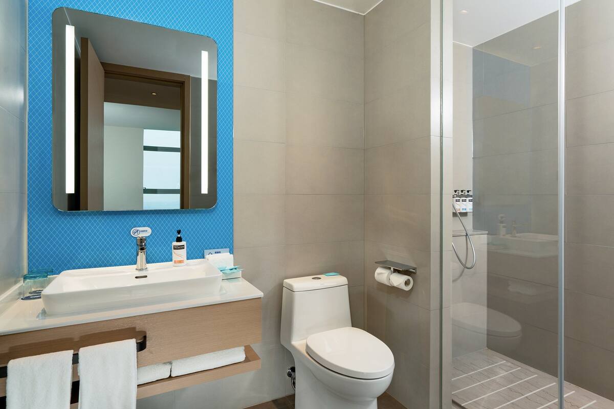 A modern bathroom with a white sink, mirror, and toilet. It features a glass shower enclosure and blue patterned wall tiles.