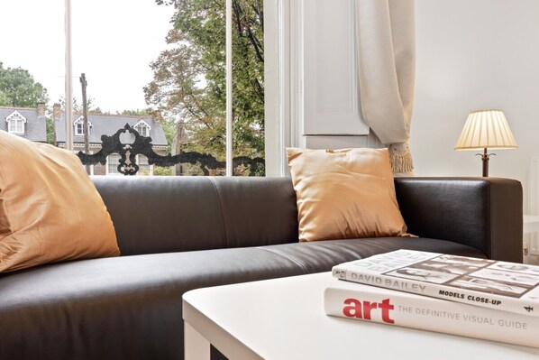 A modern living room with a black leather sofa, beige cushions, a white side table, and a book titled "art THE DEFINITIVE VISUAL GUIDE".