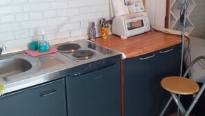 Eine kleine Küche mit Spüle, Herd, Mikrowelle und einem Hocker.