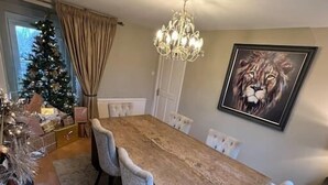 A dining room with a wooden table, white chairs, a chandelier, a Christmas tree, and a lion painting on the wall.