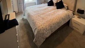 A bedroom with a bed, bedside tables, a lamp, a window with curtains, and a ceiling light.