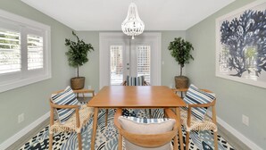 A dining area with a wooden table, chairs with patterned cushions, a chandelier, and potted plants. - The Ivanhoe Hideaway (Sarasota)