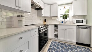 A modern kitchen with white cabinets, stainless steel appliances, and a patterned rug. - The Ivanhoe Hideaway (Sarasota)