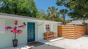 A small, light green building with a blue door, a bench, and a potted plant with pink flowers. - The Ivanhoe Hideaway (Sarasota)