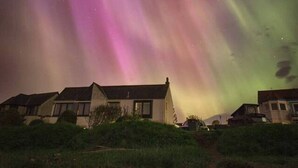 Un quartier résidentiel avec des maisons, sous un ciel nocturne illuminé par les aurores boréales.