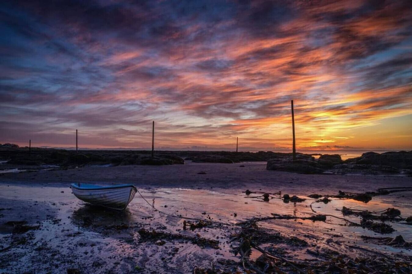 Een strandscène met een boot in het zand en een ondergaande zon op de achtergrond.