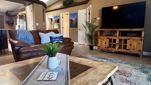 A living room with a brown leather couch, a coffee table with a plant, a TV, and a wooden entertainment unit. - Private Backyard w/Outdoor Kitchen & Boat Parking! (Lake Havasu City)