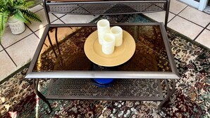 Un divano marrone imbottito con due cuscini a tema farfalla, un tavolino in vetro con tre candele bianche e un tappeto decorato.